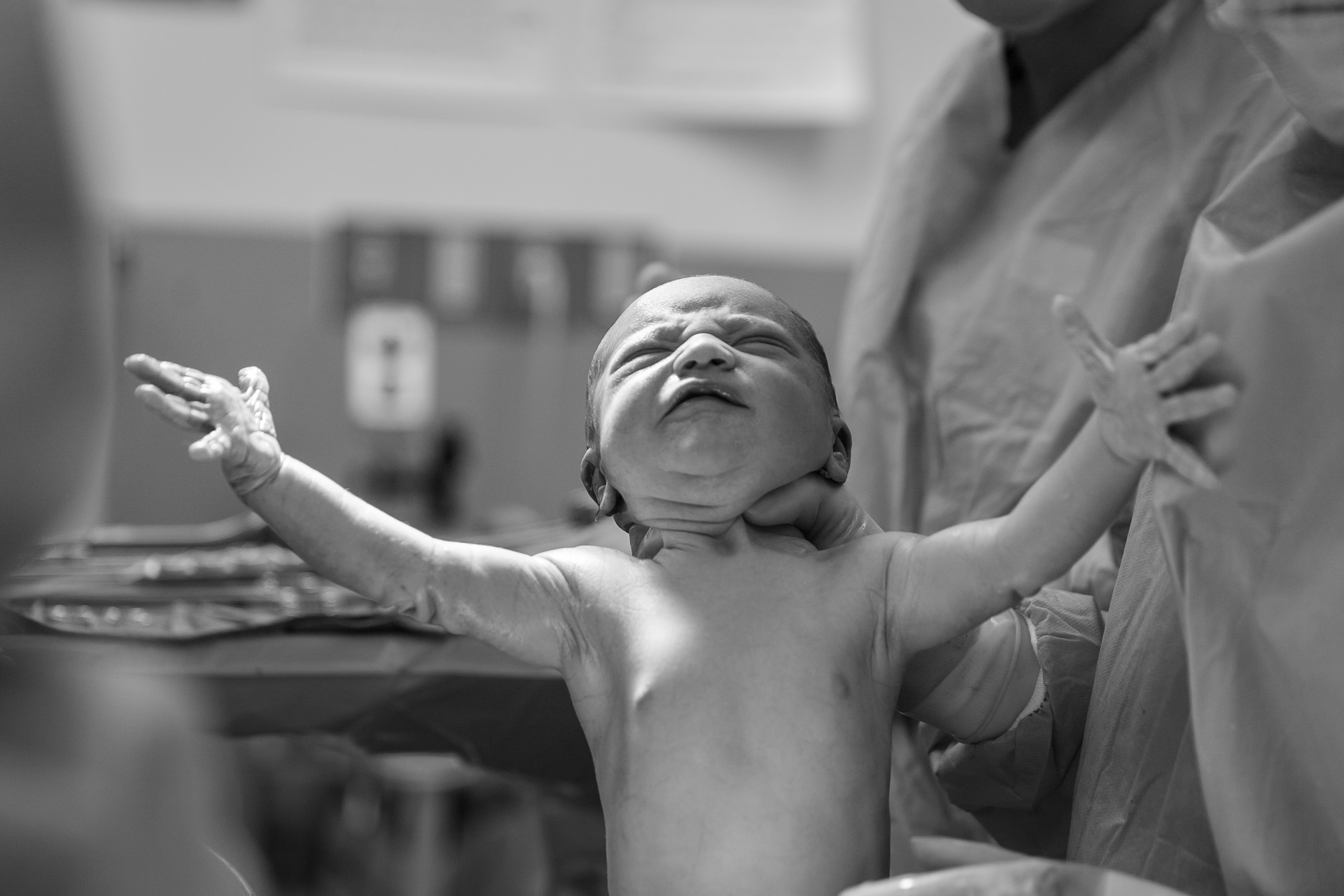 black & white image of a baby just being born, who is being held up by health care providers. Photo by Alex Hockett on Unsplash
