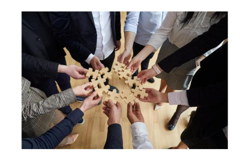 people in a circle with outstretched hands holding puzzle pieces - trying to connect the puzzle pieces together