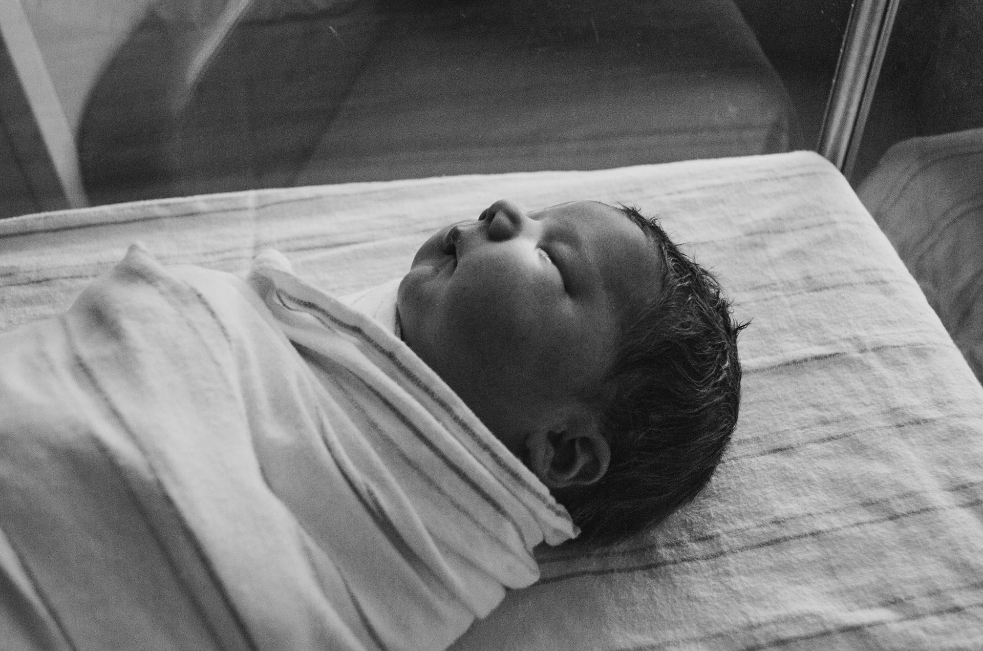 black & white image of sleeping newborn baby swaddled in a blanket. Photo by Kelly Sikkema on Unsplash.